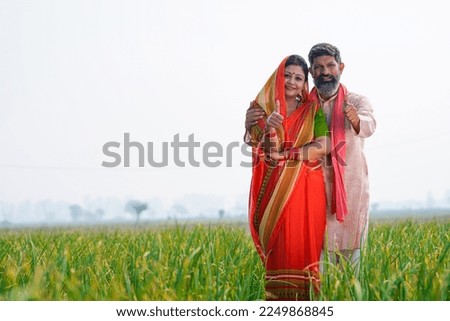 Indian farmer couple standing together and showing thumps up at agriculture field.