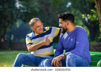 Indian father showing thumps up with young son at park.
