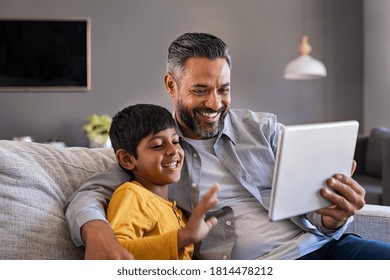 Indian father and smiling son sitting on couch using digital tablet at home. Man and boy using tablet for video calling at home. Middle eastern dad with son doing videocall during quarantine. - Powered by Shutterstock