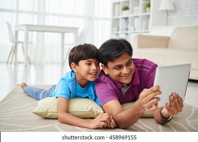 Indian father and son lying on floor and watching cartoons on digital tablet