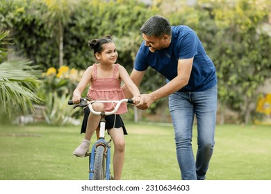 Indian father teaching riding a cycle to his daughter in lawn - Powered by Shutterstock