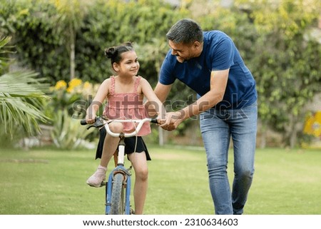 Indian father teaching riding a cycle to his daughter in lawn