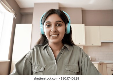 Indian female college student teacher wearing headphones looking at web cam distance learn or teach online. Web lesson video call remote class, online job interview concept. Headshot. Webcam view.