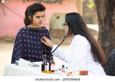 Indian female doctor checking young adult girl patient heartbeat with stethoscope at village outdoor, woman getting examine by medical person, Rural India healthcare concept