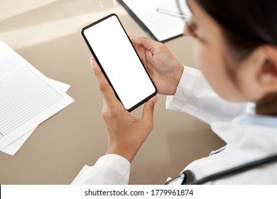 Indian Female Doctor Holding In Hands Using Cell Phone App Mock Up White Screen, Over Shoulder Closeup View. Healthcare Telemedicine Online Consultation, Remote Mobile Medical Smartphone Application