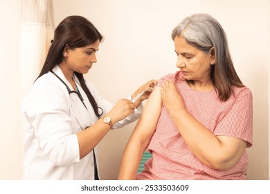 Indian female doctor make arm injection to positive senior female patient in hospital, caring woman doctor vaccinate smiling mature woman in clinic, vaccination, elderly healthcare concept - Powered by Shutterstock