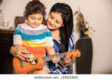 Indian Female Music Teacher Teaching Acoustic Guitar Or Ukulele To Little Girl At Home,Child Learning Guitar From Her Mother. Skill India.