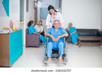 Indian Female Nurse Or Medical Staff Helping Disabled Elderly Man Patient In Wheelchair At Hospital, Doctor With Old Person, Healthcare Concept.