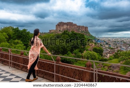 An Indian Female Solo Traveler enjoying the view of Mehrangarh Fort with Blue Cityscape from Jaswant Thada at Jodhpur, Rajasthan, India. 