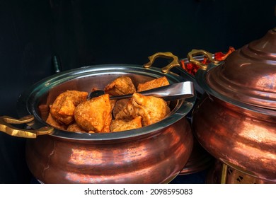 Indian food samosa in a large copper pot on the counter of an outdoor cafe. Crispy fried triangle patties.
