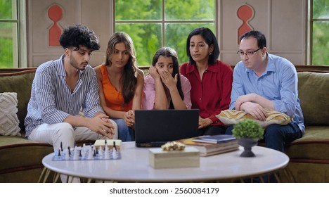 Indian frightened family group use laptop watch scary horror scene in  movie feels fear closed eyes spend time indoor house. Young adult girl boy sitting on cozy sofa couch look thriller show together - Powered by Shutterstock