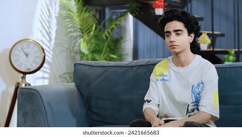 Indian frustrated teenager boy sitting sofa feeling bad anger heartbroken hurtful relationship indoor home. sad teen age one worried alone man suffer think fear tension regret mistake uncertain future - Powered by Shutterstock