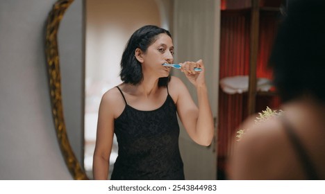 Indian gen x old aged smiling woman reflected look bathroom mirror hold toothbrush brushing healthy white teeth clean mouth with toothpaste do morning day dental care daily routine indoor home - Powered by Shutterstock