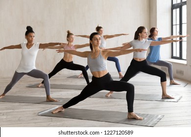 Indian girl and diverse group of young sporty people practicing yoga, doing Warrior II exercise, Virabhadrasana 2 pose, working out, indoor full length, female students training at sport club, studio - Powered by Shutterstock