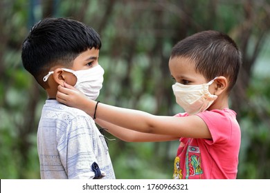 Indian girl helping brother wearing face mask to prevent covid-19. sister taking care of brother during corona virus pandemic. Teaching to wear mask properly. How to wear face mask.