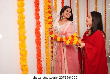 An Indian girl and her sister decorate their house with marigold flowers - an Indian festival, Diwali celebration. Two beautiful girls dressed in ethnic wear for the festival of Diwali 