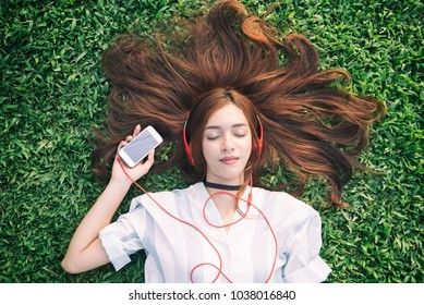 Indian Girl Listening To Music Streaming With Headphones From Smartphone In Summer On A Meadow.