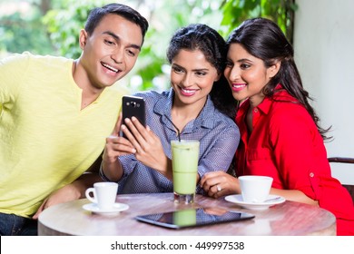 Indian girl showing pictures on smart phone to her friends in an Indian cafe - Powered by Shutterstock