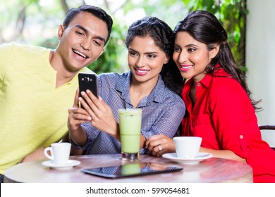 Indian girl showing pictures on smart phone to her friends in an Indian cafe - Powered by Shutterstock