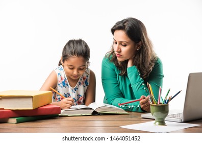 Indian girl studying with mother or teacher at study table with laptop computer, books and having fun learning