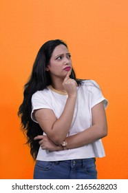 Indian girl thinking with finger on chin looking at right side with copy space. Beautiful Indian girl or Young south Asian woman thinking something deep isolated on orange background.