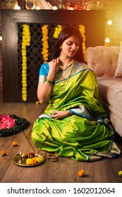 Indian Girl / women holding Pooja Thali while wearing green saree and sitting at home with flower rangoli and Samai, celebrating Diwali or hindu festival. selective focus