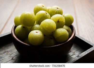 Indian gooseberry or Amla (Phyllanthus emblica) in a wooden bowl over colourful or wooden background, selective focus


