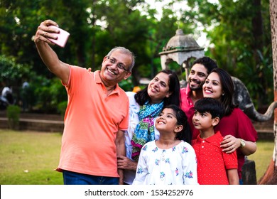 Indian Grandfather Taking Selfie - Multi Generation Asian Family Of Six, Capturing Family Photograph In Smartphone While Standing In Garden / Park