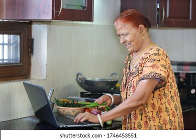 Indian Grandmother Learning Online To Cook Dishes. Technology In Learning.Technology In Kitchen. Technology In Daily Life. Old Lady Happy Using Internet And Laptop In Kitchen. Happiness Of Learning. 