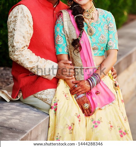 Indian Groom In Golden Sherwani and Red Waistcoat with Bride in Yellow Lehenga, Blue Blouse and Pink Dupatta