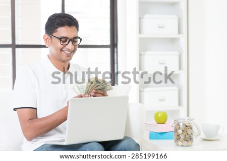Indian guy counting cash, earning money from his successful online business. Asian man working from home.