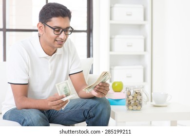 Indian Guy Counting Money And Smile At Home. Asian Man Holding Cash Indoor.