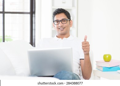 Indian Guy With Laptop Computer Working From Home And Giving Thumb Up. Asian Man Using Internet Indoor, Relaxed And Sitting On Sofa. Handsome Male Model.