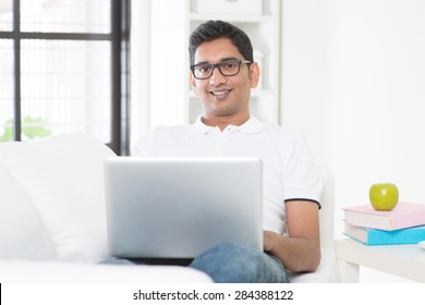 Indian Guy With Laptop Computer Working From Home. Asian Man Using Internet Indoor, Relaxed And Sitting On Sofa. Handsome Male Model.