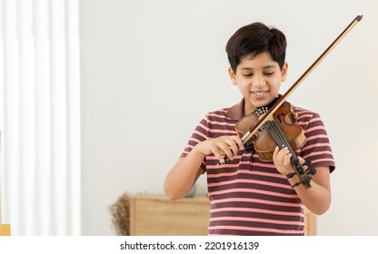 Indian Handsome Teenage Boy, Playing, Practicing Violin Musical Instrument With Happiness In Bedroom At Cozy Home In Leisure Time, Smiling, Having Copy Space. Education, Lifestyle, Creativity Concept