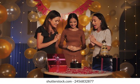 Indian happy beautiful young adult female friends standing sing song excited teen girl burning candles on birthday cake enjoying festive party day celebration together indoor light decor home - Powered by Shutterstock