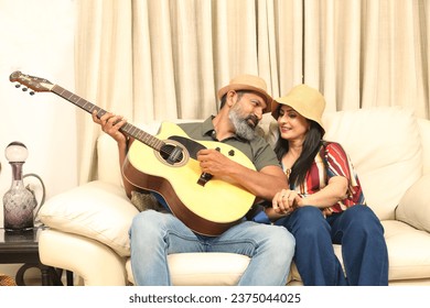 Indian happy Couple Plays Guitar and Sing Song in Living Room sitting on the sofa at home. while young husband playing guitar in living room. Concept : Music and Lifestyle. - Powered by Shutterstock