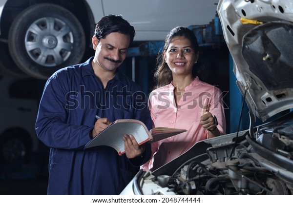 Indian happy female customer showing thumbs\
up for repairing her car on time. Portraying customer trust and\
satisfaction towards the service station standing and briefing the\
car specialist.