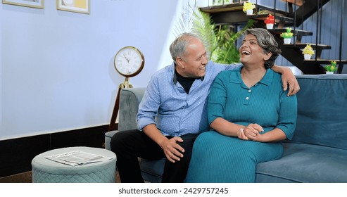 Indian happy middle aged old husband wife sitting on comfy sofa couch making funny communication at indoor home. Smiling older senior couple enjoying romantic talking together summer vacation holiday  - Powered by Shutterstock