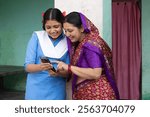 Indian happy rural mother and young daughter using mobile phone at home in village. Student rural girl using phone with mother