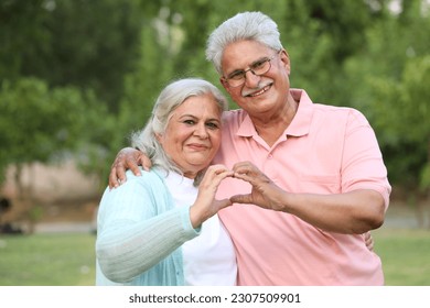 Indian happy senior couple making and showing heart with hands in garden  - Powered by Shutterstock