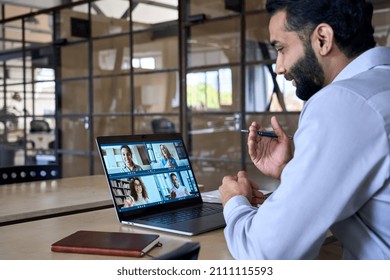 Indian happy smiling businessman ceo having working videocall on planning finance with multiracial team colleagues using laptop pc in modern corporation office. Over shoulder view. - Powered by Shutterstock