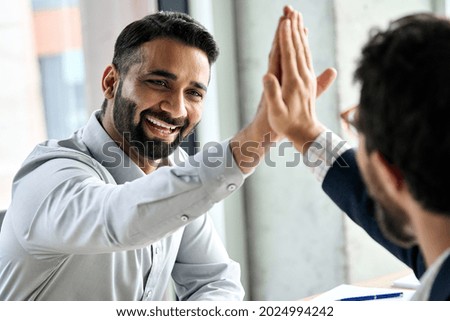 Indian happy smiling multiracial professional ceo businessman giving highfive to business partner after financial acquisition bank bargain contract at office. High five concept. Over shoulder view.