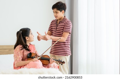 Indian happy teenage boy, girl sibling teaching, learning, playing, practicing violin musical instrument together at cozy home in leisure time, smiling. Education, Lifestyle, Creativity Concept. - Powered by Shutterstock