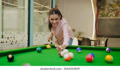 Indian happy young adult gen z alone business woman hold cue stick hit ball play billiards snooker game office after work. Teen age female corporate enjoy break time have fun joy indoor job place - Powered by Shutterstock