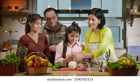 Indian happy young adult mature mother father standing with teen girl child teach to cut fresh vegan slice on chop board prepare healthy food enjoy learn together spend day time indoor modern kitchen - Powered by Shutterstock