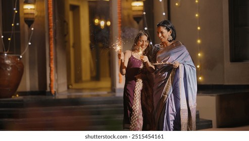 Indian Hindu happy family in traditional clothes play firecrackers celebrate festive season outdoor home. Smiling mother with young adult daughter enjoy Diwali festival with parent outside house - Powered by Shutterstock