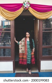 Indian Housewife Stands At The Door Step To Welcome The Guest Coming To The House. Woman Home Owner Waiting At The Doorstep As People Arrive At Her Home.