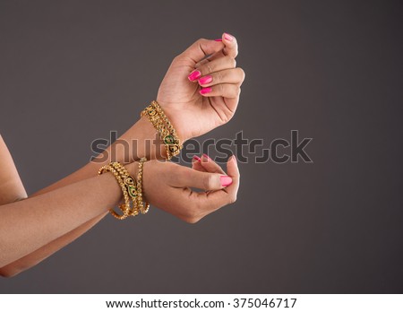 Indian Jewellery - Closeup of girl wearing traditional designer gold bangles/bracelets and showing graceful dance poses of hand over dark background, selective focus