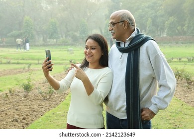 Indian Joyful Grand Father Looking Into The Mobile With Her Grand Daughter. They Both Look Happy And Cheerful.